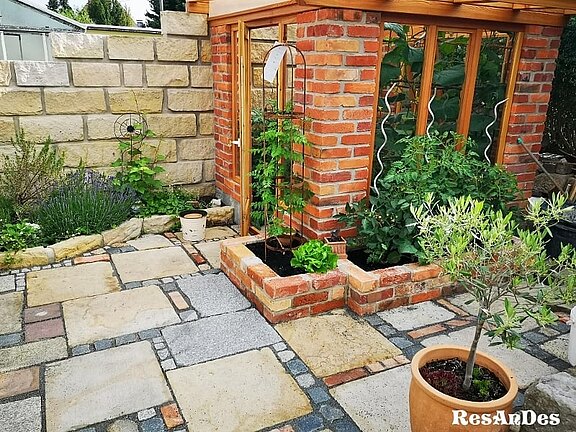 Kombination aus historischen Ziegeln für das Gartenhäuschen und Sandstein-Gehwegplatten für die Terrassengestaltung